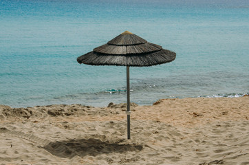 Straw sunshade, parasol, beach umbrella on sandy beach and sea background. Cyprus, Mediterranean Sea. Summer, travel, beach vacation concept. Copyplace, place for text