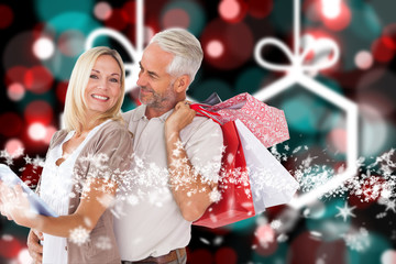 Happy couple with shopping bags and tablet pc against blurred christmas background