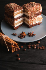 Sweet dessert tiramisu in a cut on a gray plate on a black wooden background with spices: cinnamon sticks and badan, coffee beans