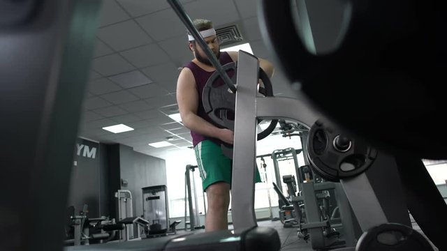 Fat man adding extra weight plates for barbell lifting, strong muscles, workout