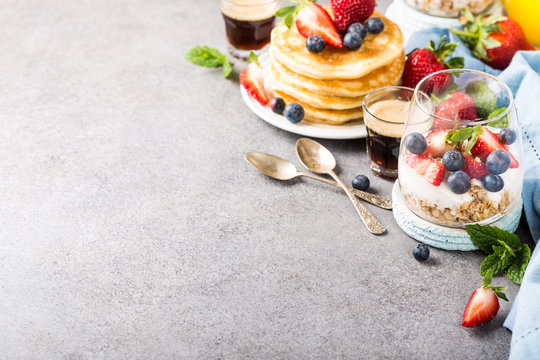 Oatmeal granola with berries and yogurt and panccakes on light gray concrete background. Healthy breakfast food concept with copy space.