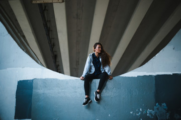 hipster woman sitting on ground under bridge