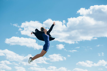 Fototapeta na wymiar a woman jumping high, wearing a blue dress against the blue sky with clouds. A woman is flying against the sky
