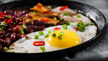 fried egg with bacon and red beans in a frying pan on wooden table