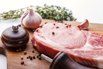 Raw pork steak, a bunch of fresh thyme, garlic, pepper peas and pepper mill on a wooden cutting...