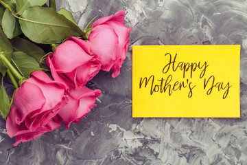 Pink roses and yellow card with an inscription, Happy Mother's Day, on a gray concrete background