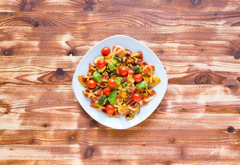 Italian pasta farfalle in tomato sauce and various type of vegetables on a wooden background, free space for text.