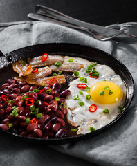 fried egg with bacon and red beans in a frying pan on wooden table