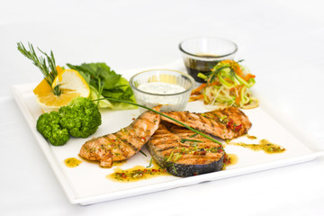 Steaks of salmon, grilled. Served with vegetables and spices on a white plate