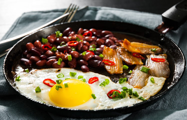 fried egg with bacon and red beans in a frying pan on wooden table