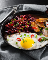 fried egg with bacon and red beans in a frying pan on wooden table