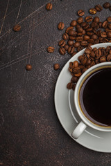 Coffee beans and coffee in a white cup on dark rusty background. Top view, copy space