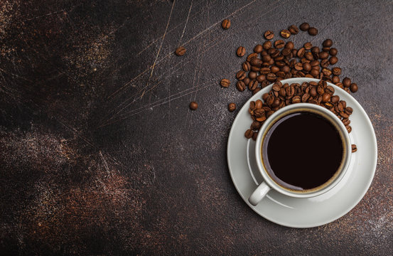 Coffee beans and coffee in a white cup on dark rusty background. Top view, copy space