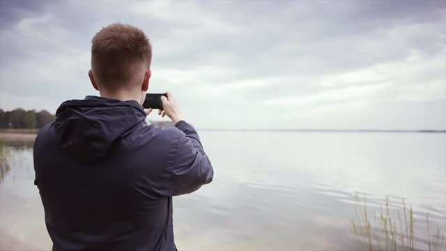 Back view of a young man tourist taking photo of sea. Traveler man taking photo with mobile phone. Take beautiful seascapes to your phone.