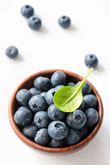 Blueberries with green leaf in bowl on white background. Closeup view, selective focus
