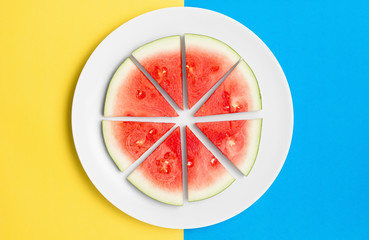 Cut watermelon on round plate with contrasting split color background.