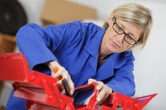 middle-age woman in coveralls doing repairs with her tool-box