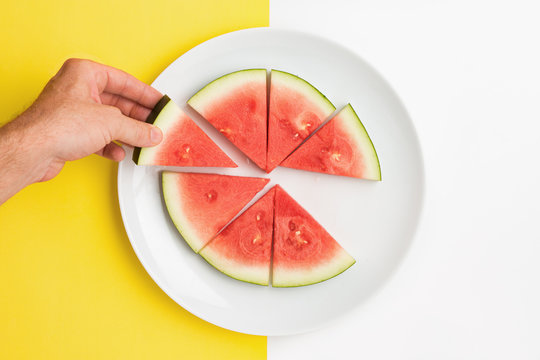 Hand holding slice of watermelon over split color background.