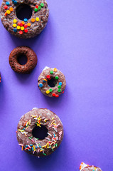 Chocolate baked doughnuts on a violet background glazed and decorated with confetti. Top view.
