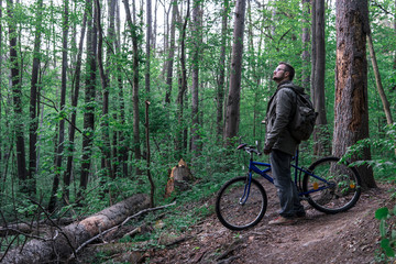 Fototapeta na wymiar Young man with backpack and glasses standing with bicycle on the forest path of the park and looking, active lifestyle concept, sport and jorney, travel surviver concept