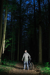 Obraz premium the guy with the bike stands out at night in the woods