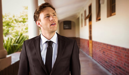 Young businessman thinking and looking up against hallway