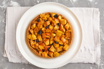 Whole vegan apple pie with cinnamon, raisins and caramel, gray background, top view