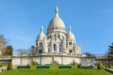 Front view of the bright white basilica of the Sacred Heart of Paris, situated at the top of the Montmartre hill, seen from the Louise Michel park by a sunny spring morning.