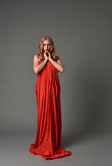 full length portrait of woman wearing red silk gown, on grey studio background.