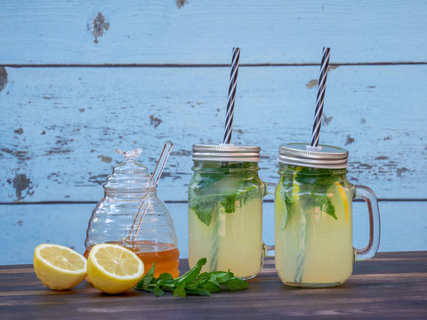 Two jars of fresh lemonade with sparkling water, mint and honey, set on a dark oak table, with a blue barn wall .in the background