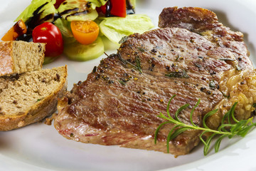 Ripened seasoned beef rump or striploin steak cooked on white plate with salad and home made bread