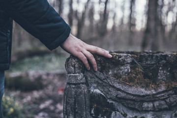 Man hand on ancient tombstone covered with moss, sorrow and eternal memory for dead people concept