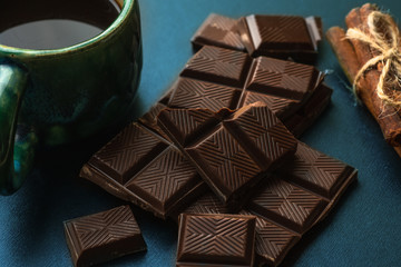 Broken bar of chocolate, cinnamon and cup of coffee an black table, close up