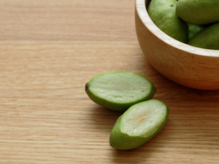 A group of green hog plums fruit, which look like small mango, in wooden bowl over bright wooden background with concepts of wellness and healthy, rich in natural antioxidants, vitamins and minerals