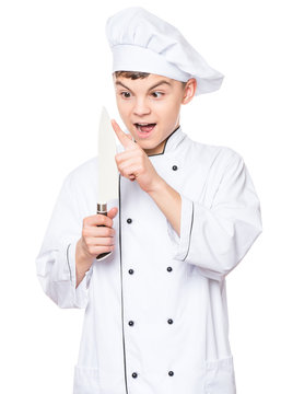 Handsome teen boy wearing chef uniform. Portrait of a cute male child cook with big knife, isolated on white background. Food and cooking concept.