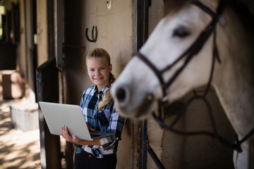 Teenage girl using laptop in the stable