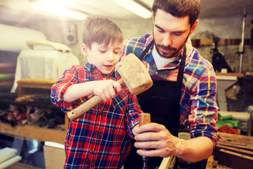 family, carpentry, woodwork and people concept - father and little son with hammer and chisel working with wood plank at workshop