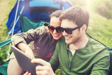 travel, hiking, technology, tourism and people concept - smiling couple with tablet pc computer sitting on chairs at camping tent