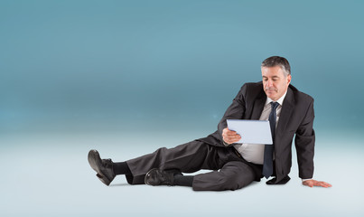 Mature businessman sitting using tablet against blue vignette background