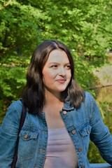 Fototapeta premium a young woman in a denim jacket stands in the park and looks to the side