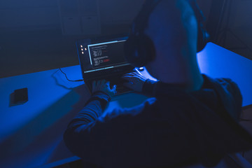 cybercrime, hacking and technology concept - male hacker with headphones and coding on laptop...