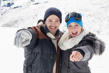Fototapeta na wymiar Cheerful couple in jackets pointing at camera on snow covered landscape