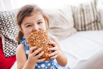 A small girl at home eating a loaf of bread.