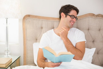 Smiling relaxed man reading book in bed