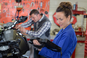 Woman holding computerised device in motorcycle garage