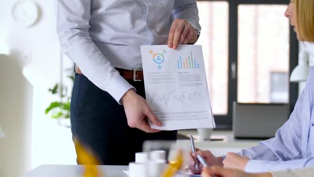 business, corporate and people concept - businessman showing papers with charts to businesswomen at office meeting or presentation