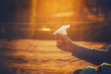 Paper airplane in man's hand at orange sunset