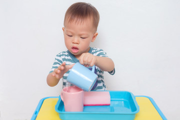 Cute little Asian 18 months old toddler boy child having fun pouring water into cup, Wet Pouring Montessori Preschool Practical Life Activities, Fine Motor Skills, Kid Sense Child Development concept