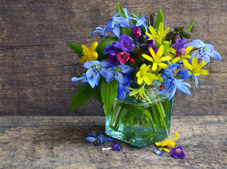 Beautiful spring flowers bouquet in a glass vase on old wooden background with space for text.Mother's Day,Birthday or Springtime greeting card concept. Selective focus.