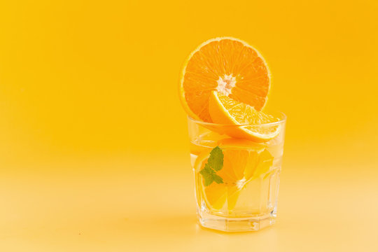Detox Water with orange in a glass on an orange background